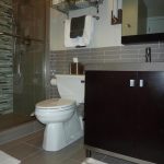 Limited Spaced Bathroom with White Closet besides dark Wood COunter on Grey Tile Wall